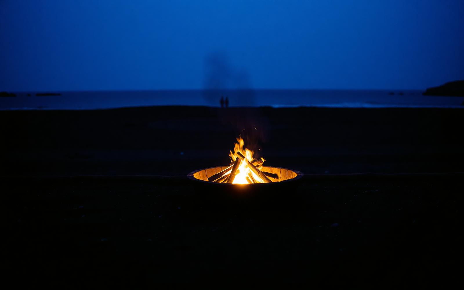 Feuerstelle an einem stillen Strand zur blauen Stunde